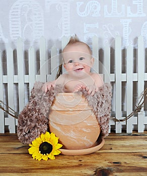 Adorable baby boy sitting in clay flower pot