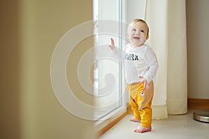 Adorable baby boy standing by the window. Toddler learning how to stand up unassisted