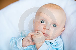 Adorable baby boy in white sunny bedroom. Newborn child relaxing in bed. Nursery for young children.