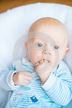 Adorable baby boy in white sunny bedroom. Newborn child relaxing in bed. Nursery for young children.