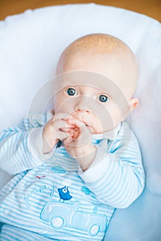 Adorable baby boy in white sunny bedroom. Newborn child relaxing in bed. Nursery for young children.