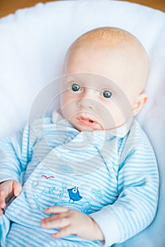 Adorable baby boy in white sunny bedroom. Newborn child relaxing in bed. Nursery for young children.