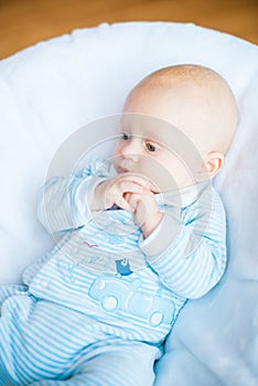 Adorable baby boy in white sunny bedroom. Newborn child relaxing in bed. Nursery for young children.