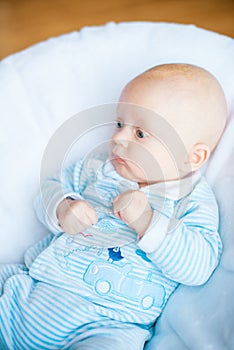 Adorable baby boy in white sunny bedroom. Newborn child relaxing in bed. Nursery for young children.