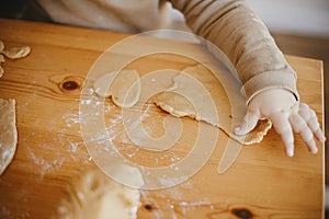 Adorable baby daughter kneading dough together with mother for gingerbread cookies on wooden table, hands close up. Cute toddler