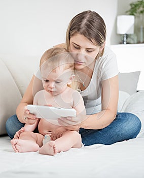 Adorable baby in diapers using tablet PC with his mother