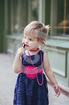 Adorable baby in a dress paints lips with lipstick