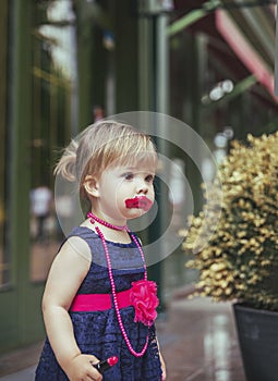 Adorable baby in a dress paints lips with lipstick