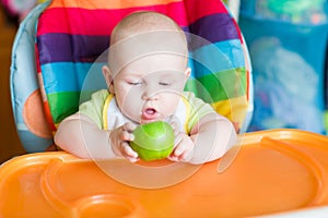 Adorable baby eating apple in high chair