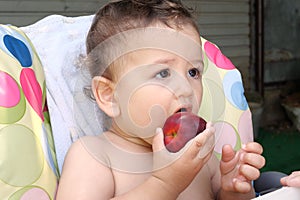 Adorable baby eating fresh orange peach. A cute little baby is sitting on the garden and is eating a peach