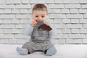 Adorable baby eating a plate of chocolate in front of a white br