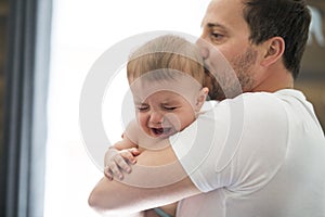 Adorable baby with father sonsoling close to the window