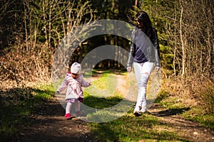 Adorable baby on forest path in nature.1 year old girl in woods with her mother