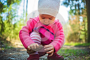 Adorable baby on forest path in nature. Portrait of 1 year old girl in woods with pine cone