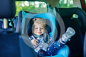 Adorable baby girl with blue eyes sitting in car safety seat. Toddler child going on family vacations and jorney