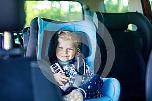 Adorable baby girl with blue eyes sitting in car safety seat. Toddler child going on family vacations and jorney. photo