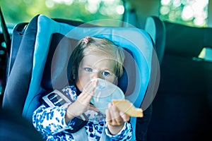 Adorable baby girl with blue eyes sitting in car safety seat. Toddler child going on family vacations and jorney