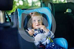 Adorable baby girl with blue eyes sitting in car safety seat. Toddler child going on family vacations and jorney