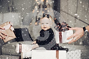 Adorable baby girl with Christmas presents. Father and mother giving her boxes with gifts from both sides of photograph.