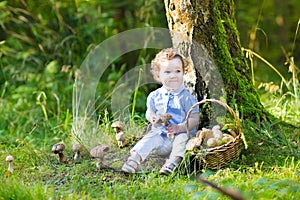 Adorable baby girl with curly hair gathering mushrooms in park