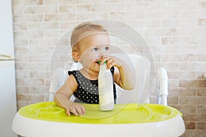 Adorable baby girl drinking milk from bottle sitting in the chair