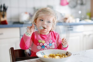 Adorable baby girl eating from fork vegetables and pasta. food, child, feeding and development concept. Cute toddler