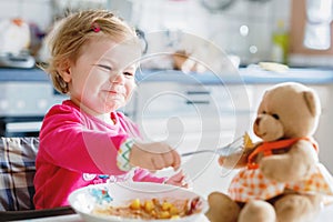 Adorable baby girl eating from fork vegetables and pasta. food, child, feeding and development concept. Cute toddler