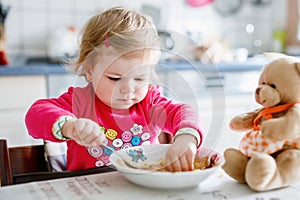 Adorable baby girl eating from fork vegetables and pasta. food, child, feeding and development concept. Cute toddler