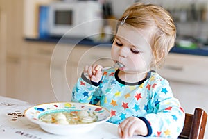 Adorable baby girl eating from spoon vegetable noodle soup. food, child, feeding and development concept. Cute toddler