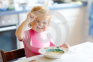 Adorable baby girl eating from spoon vegetable noodle soup. food, child, feeding and development concept. Cute toddler