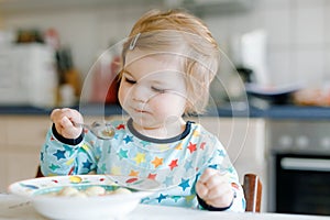 Adorable baby girl eating from spoon vegetable noodle soup. food, child, feeding and development concept. Cute toddler