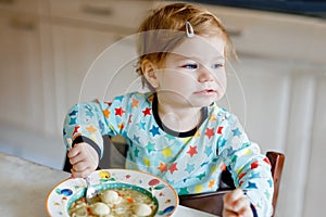 Adorable baby girl eating from spoon vegetable noodle soup. food, child, feeding and development concept. Cute toddler