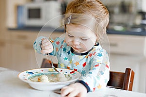 Adorable baby girl eating from spoon vegetable noodle soup. food, child, feeding and development concept. Cute toddler