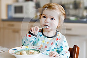 Adorable baby girl eating from spoon vegetable noodle soup. food, child, feeding and development concept. Cute toddler