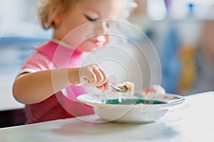 Adorable baby girl eating from spoon vegetable noodle soup. Healthy food, child, feeding and development concept. Cute