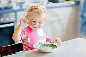 Adorable baby girl eating from spoon vegetable noodle soup. Healthy food, child, feeding and development concept. Cute