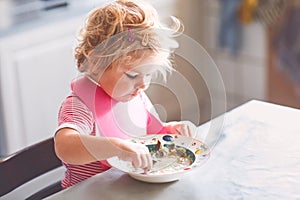 Adorable baby girl eating from spoon vegetable noodle soup. Healthy food, child, feeding and development concept. Cute