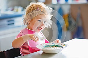 Adorable baby girl eating from spoon vegetable noodle soup. Healthy food, child, feeding and development concept. Cute