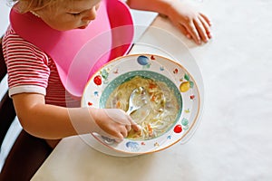 Adorable baby girl eating from spoon vegetable noodle soup. Healthy food, child, feeding and development concept. Cute