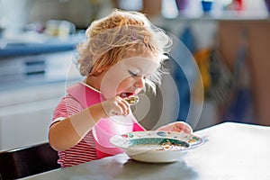 Adorable baby girl eating from spoon vegetable noodle soup. Healthy food, child, feeding and development concept. Cute