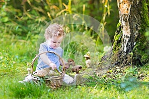 Adorable baby girl gathering mushrooms in a big basket