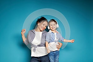 Adorable baby girl with headphones dancing near her mother hugging her on a blue background with copy space
