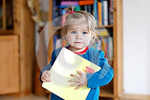 Adorable baby girl holding a book. Beautiful toddler child at home wants reading fairy tale.