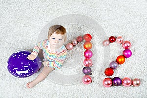 Adorable baby girl holding colorful vintage xmas toy ball in cute hands. Little child and Christmas tree balls as twelve