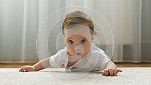 Adorable baby girl lies on her stomach on the floor, looks at the camera and smiles. Early baby development. Cute little