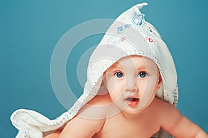 Adorable baby girl. Newborn child relaxing and laying on belly on bed with white towel on head. Nursery for young children. Textil