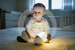 Adorable baby girl playing with bedside lamp in nursery