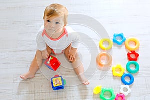 Adorable baby girl playing with educational toys in nursery. Happy healthy child having fun with colorful different toys
