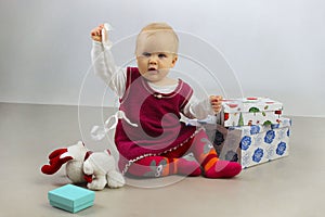 An Adorable Baby Girl in red dress playing with Christmas Gifts.