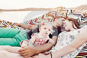 Adorable baby girl  shocked face, lying with her happy father and mother, young hipster couple relaxing with daughter in  a